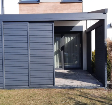 Pergola tkaninowa przyścienna o wymiarach 4,5 × 3 m, Konstrukcja w kolorze antracyt (zbliżony do RAL 7016), Całość uzupełnia zabudowa boczna shuttersy. Materiałowy dach z wodoodpornej tkaniny DRIPLUX – szary na zewnątrz i jaśniejszy od środka, Dach jest sterowany elektrycznie systemem SOMFY. Spin Szczecin